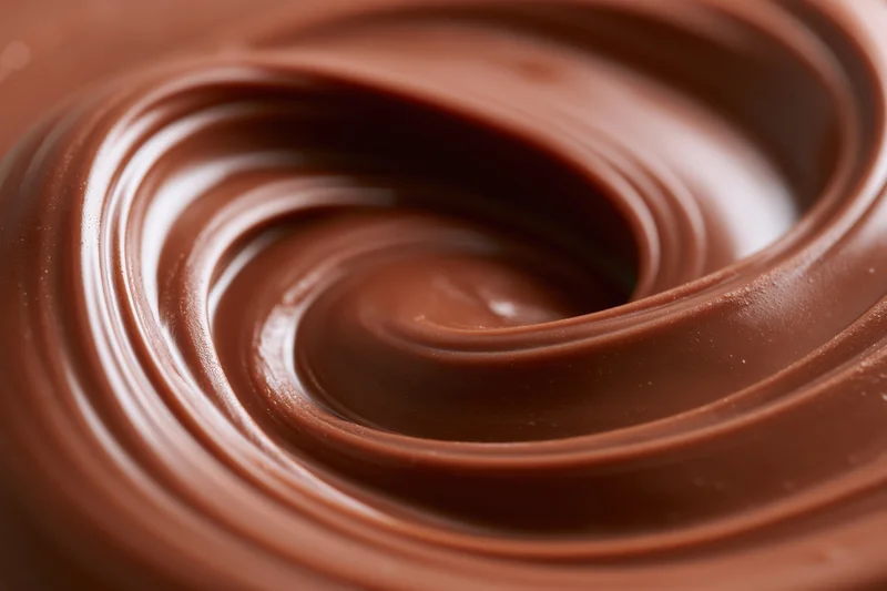 Melted milk chocolate swirled in smooth glossy pattern on flat surface