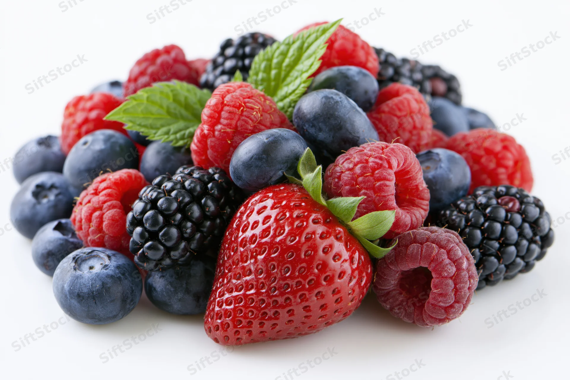 A pile of mixed fresh berries including strawberries, blueberries, raspberries and blackberries on a white background