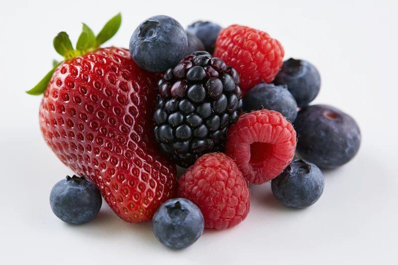 Mixed fresh berries including strawberry blueberry raspberry and blackberry arranged on white surface