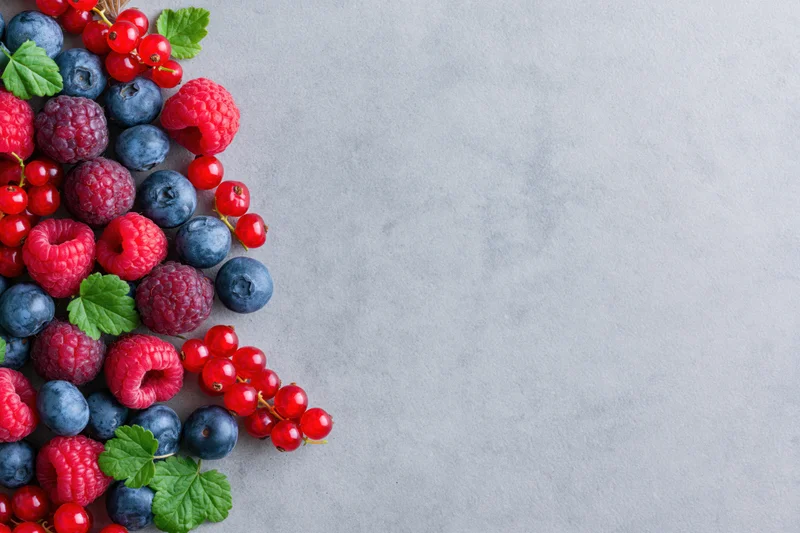 Mixed fresh berries arranged in a cluster on a gray surface with copyspace