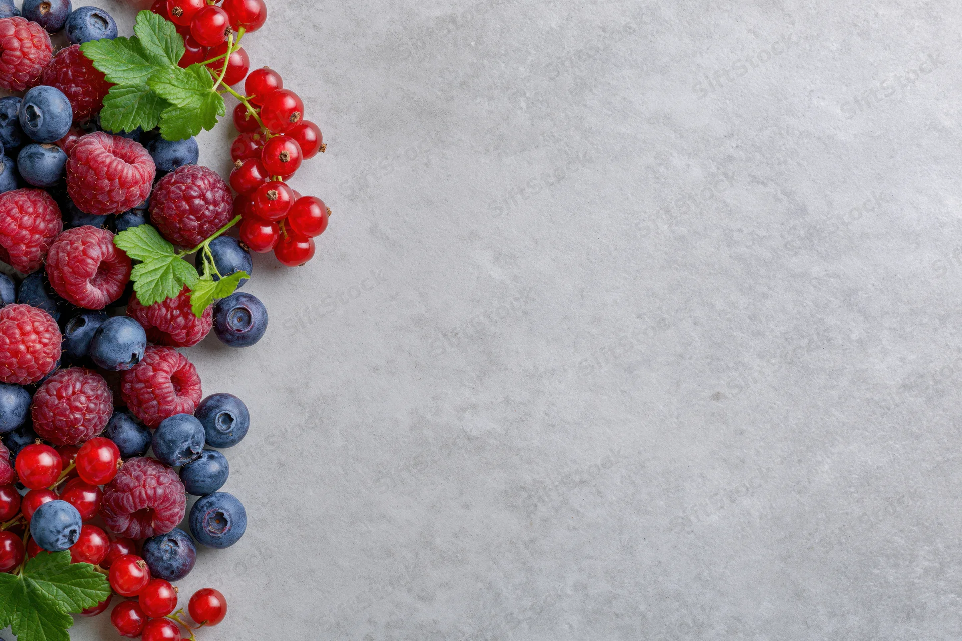 Mixed fresh berries arranged in corner on gray surface with copyspace