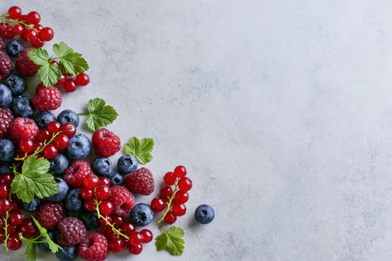 Mixed fresh berries including raspberries blueberries and red currants arranged on a light stone surface with copyspace