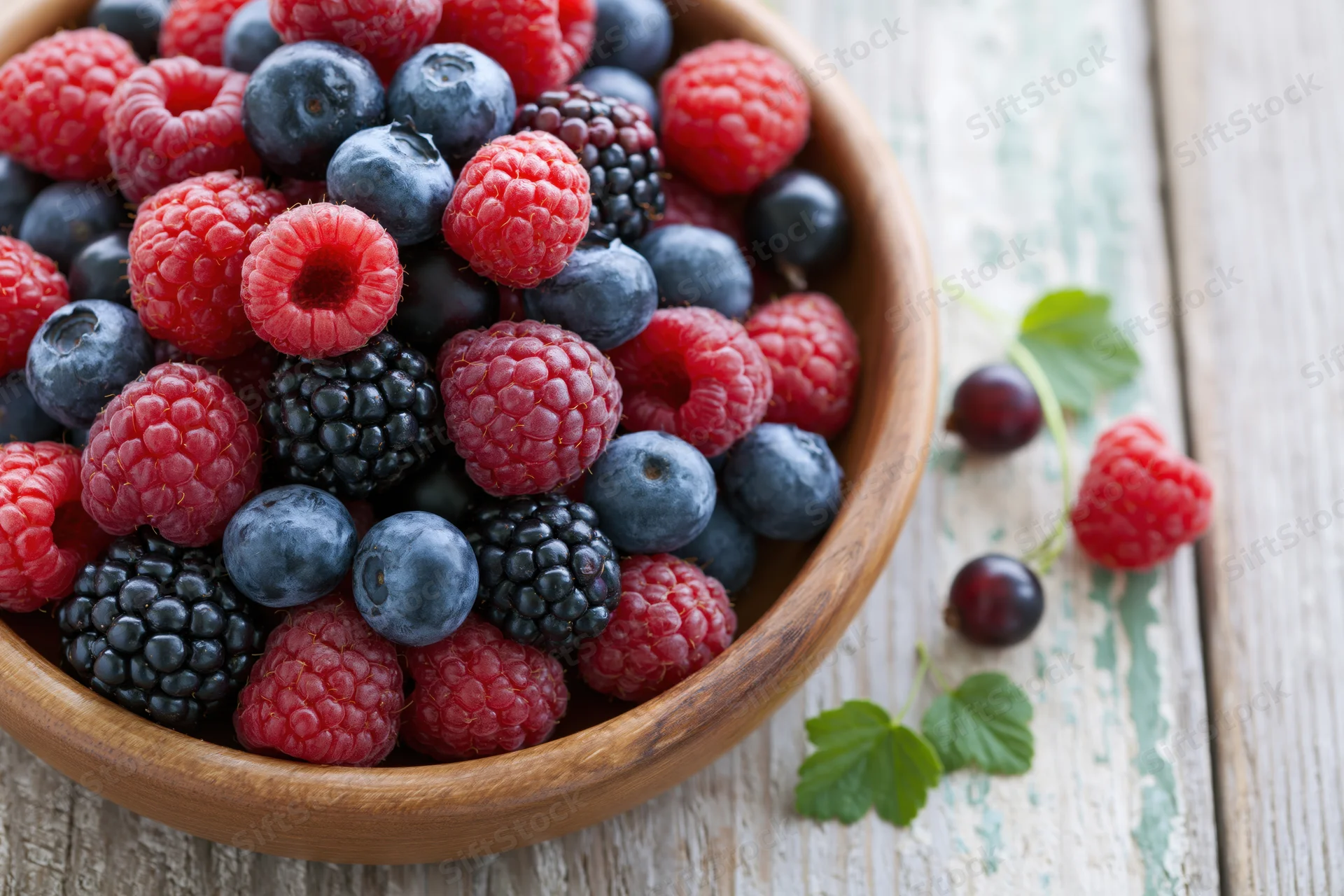 Mixed fresh berries in a wooden bowl on a rustic wooden table