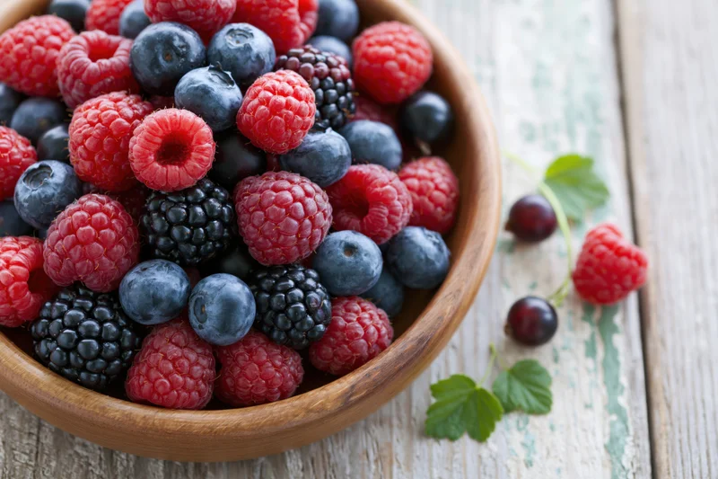 Mixed fresh berries in a wooden bowl on a rustic wooden table