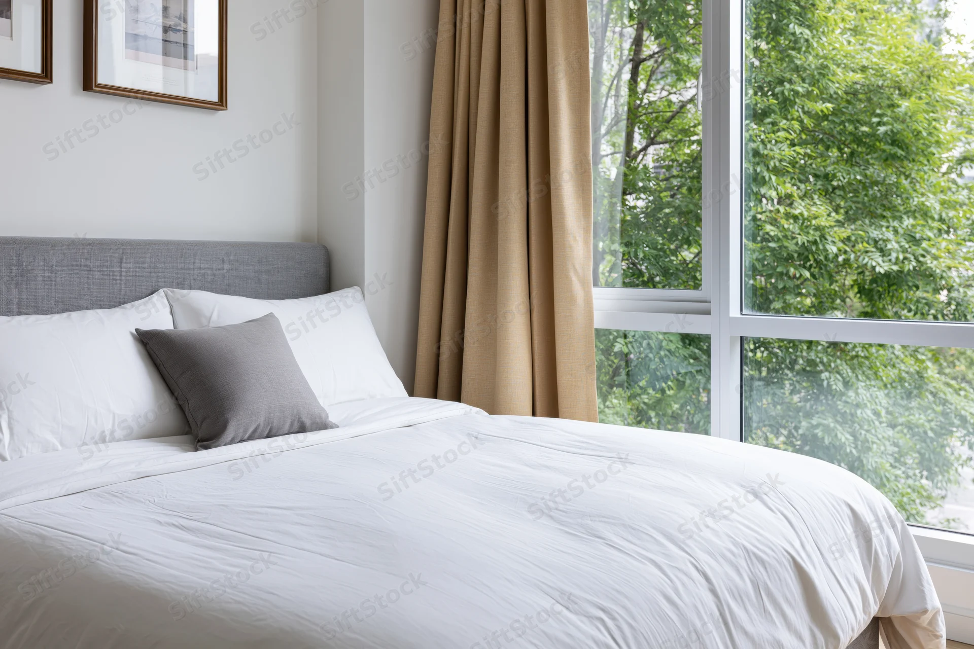 Neatly made double bed in modern hotel or condo bedroom with window view of green trees
