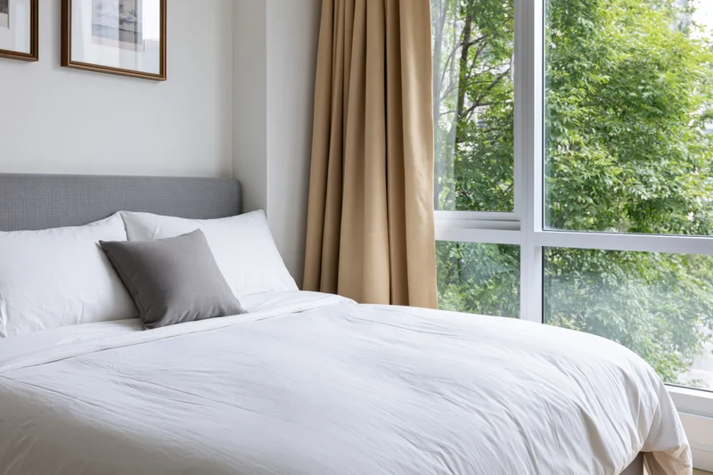 Neatly made double bed in modern hotel or condo bedroom with window view of green trees