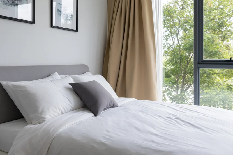 Neatly made double bed in modern hotel or condo bedroom with window view of trees