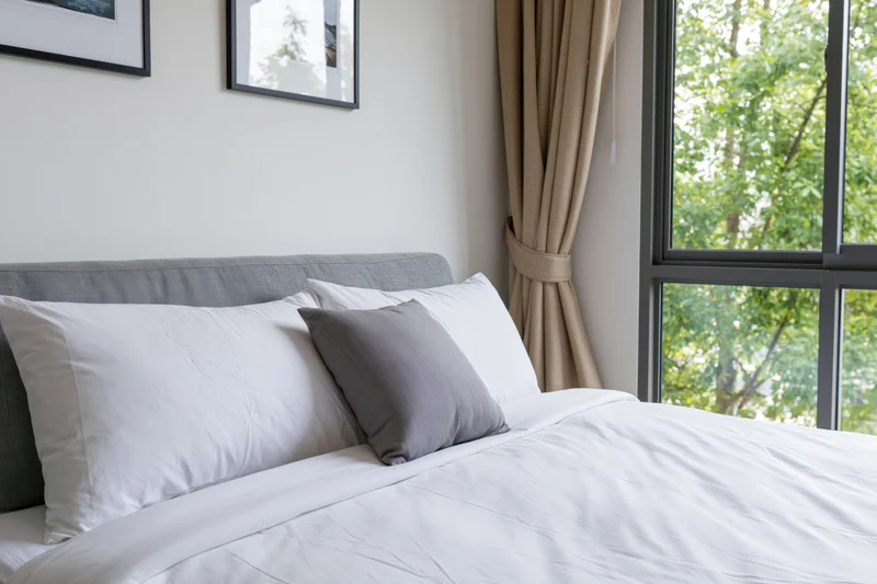 Neatly made double bed in modern hotel or condo bedroom with window view of trees