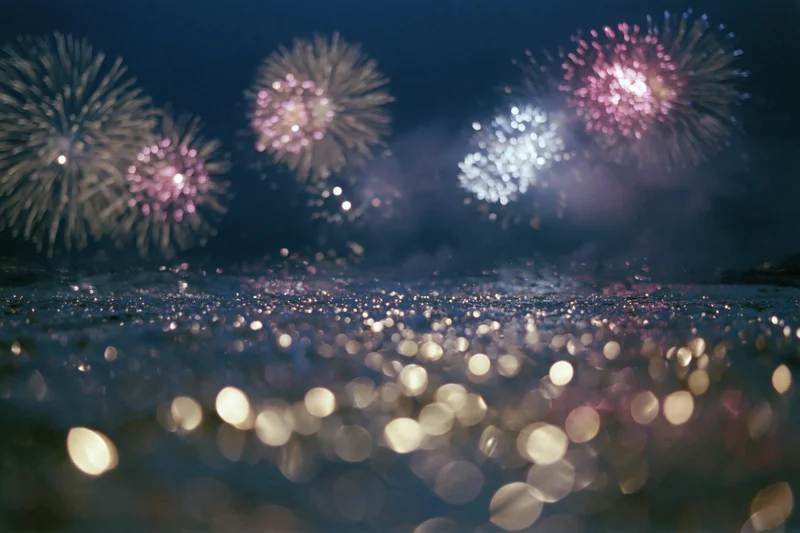 Fireworks bursting across dark night sky reflected in water below