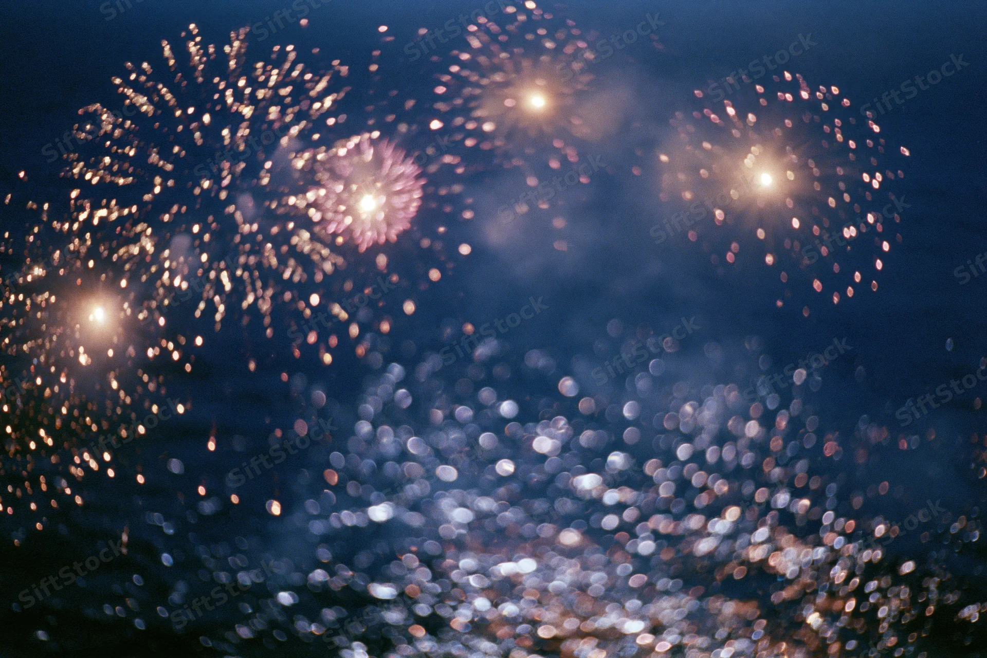 Fireworks bursting across dark night sky with reflections on water below