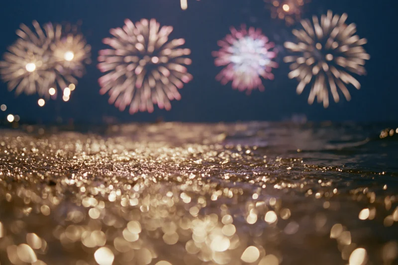 Fireworks bursting across dark night sky reflected in shimmering water surface