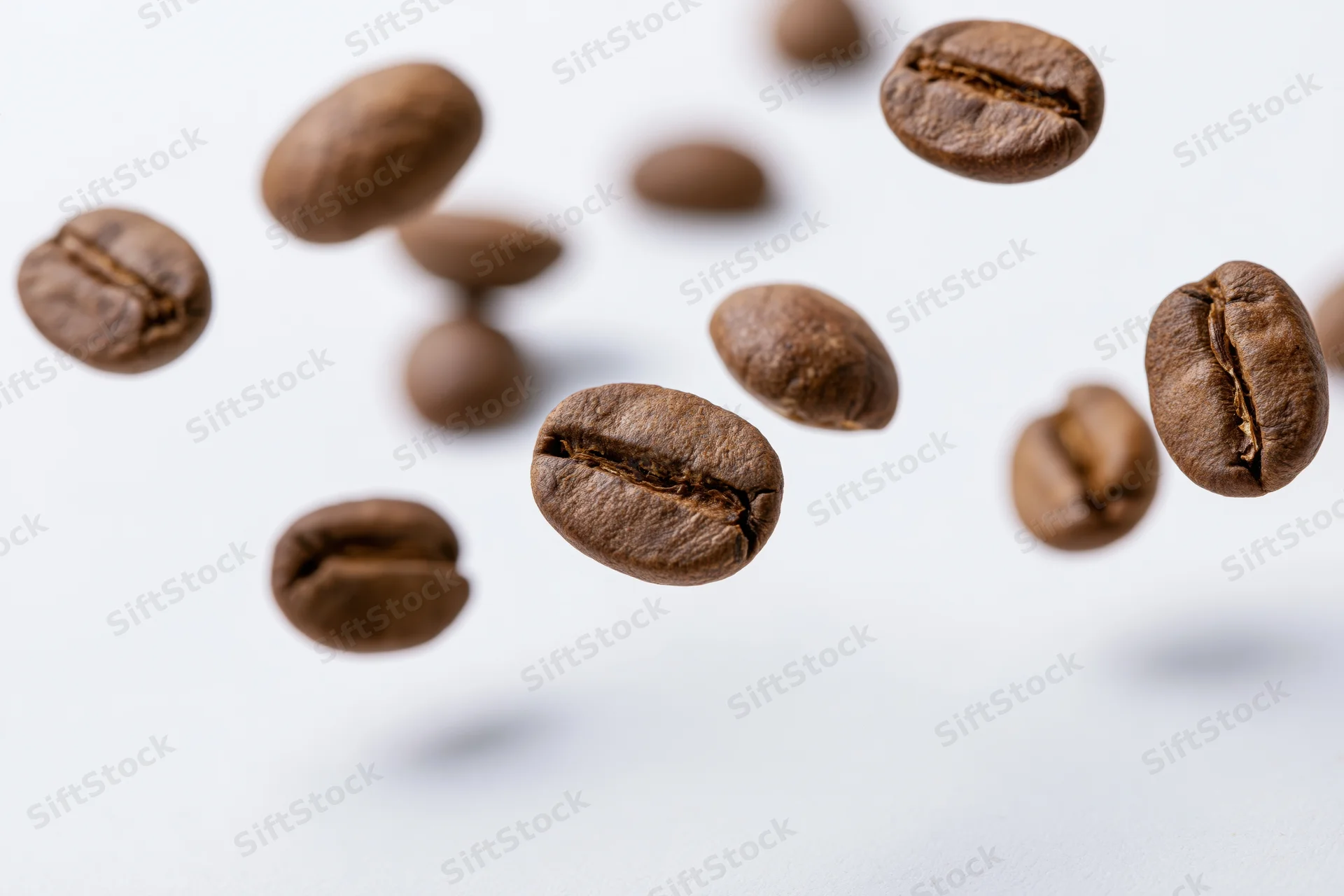 Roasted coffee beans suspended midair against a white background