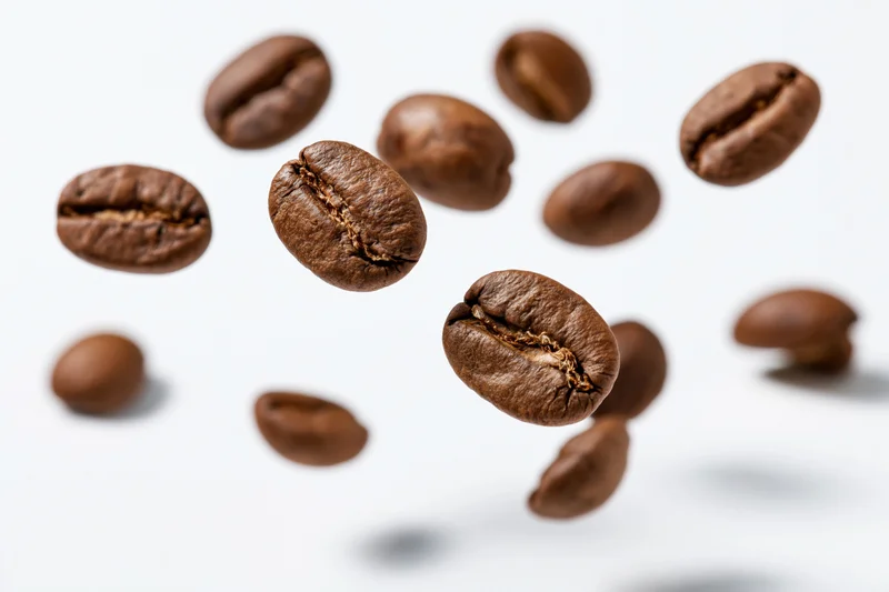Roasted coffee beans suspended midair against white background