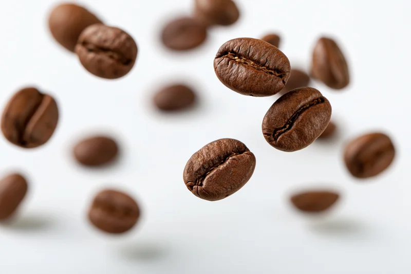 Roasted coffee beans floating midair scattered against white background
