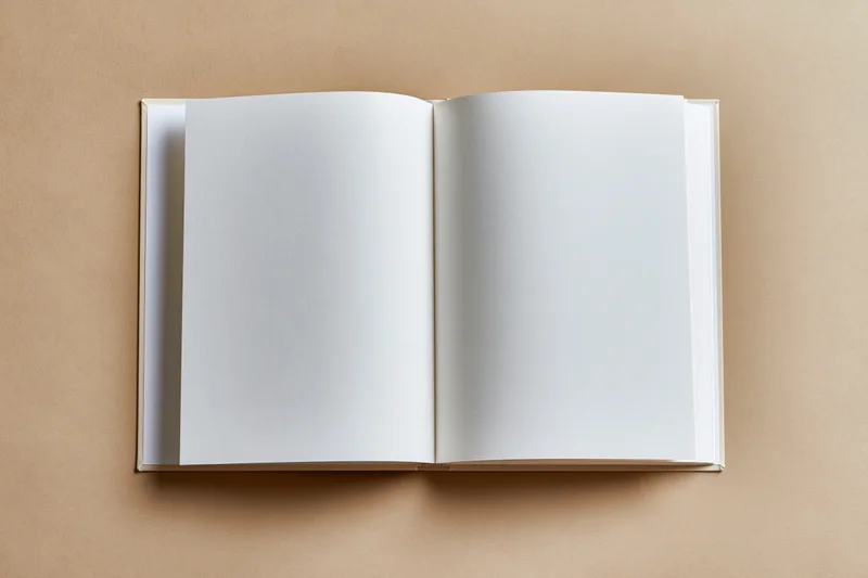 Open blank hardcover book lying flat on beige surface with empty white pages