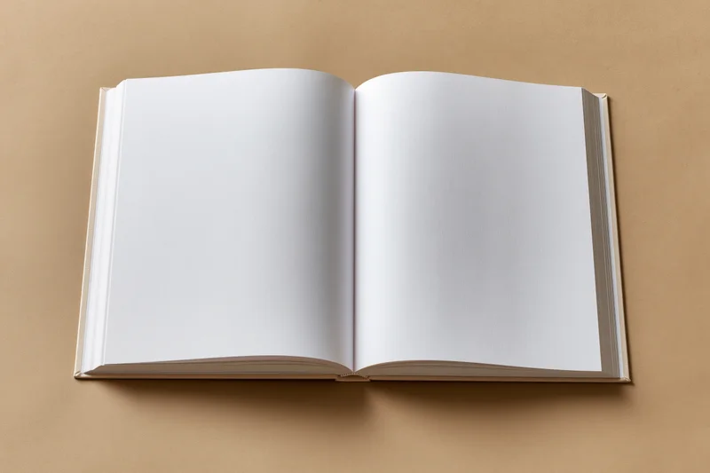 Open blank hardcover book lying flat on beige surface with empty white pages