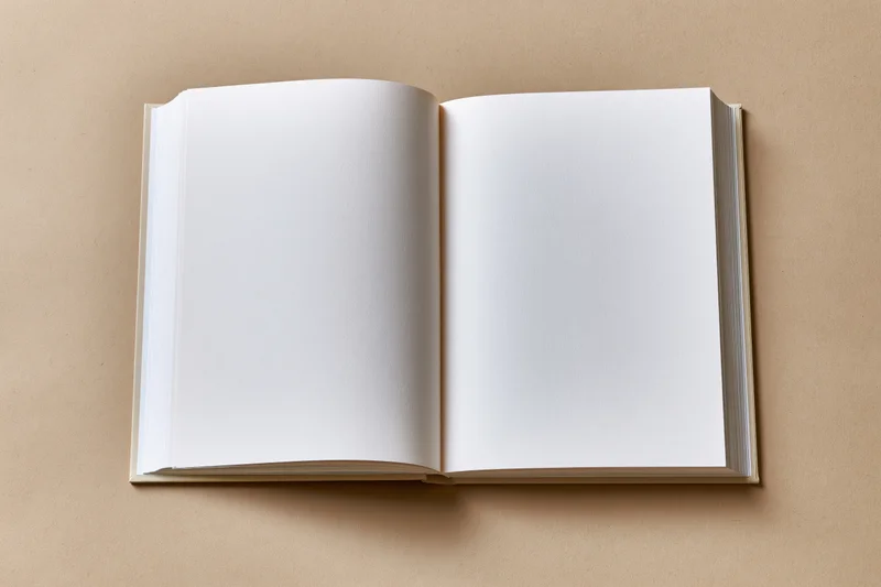 Open blank hardcover book lying flat on beige surface with empty pages for design or text placement