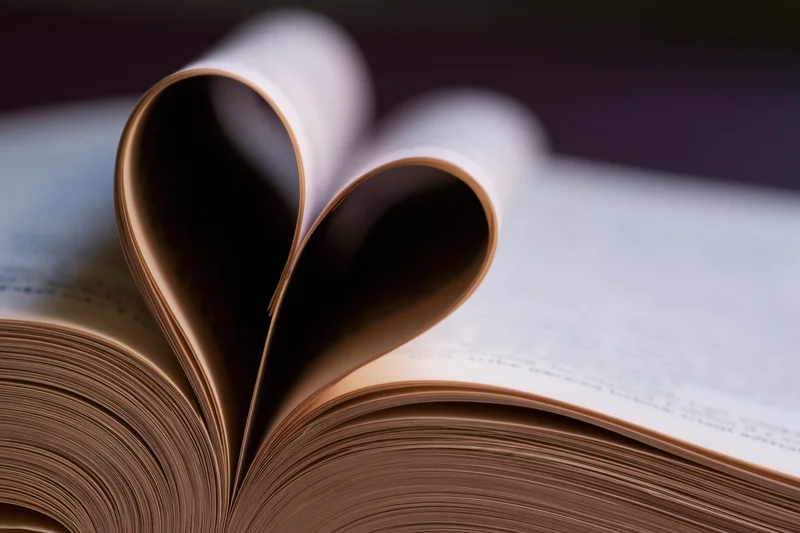 Open book with pages folded into heart shape on flat surface