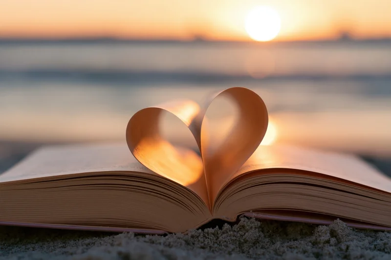 Open book with pages shaped into a heart resting on sand at sunset on a beach