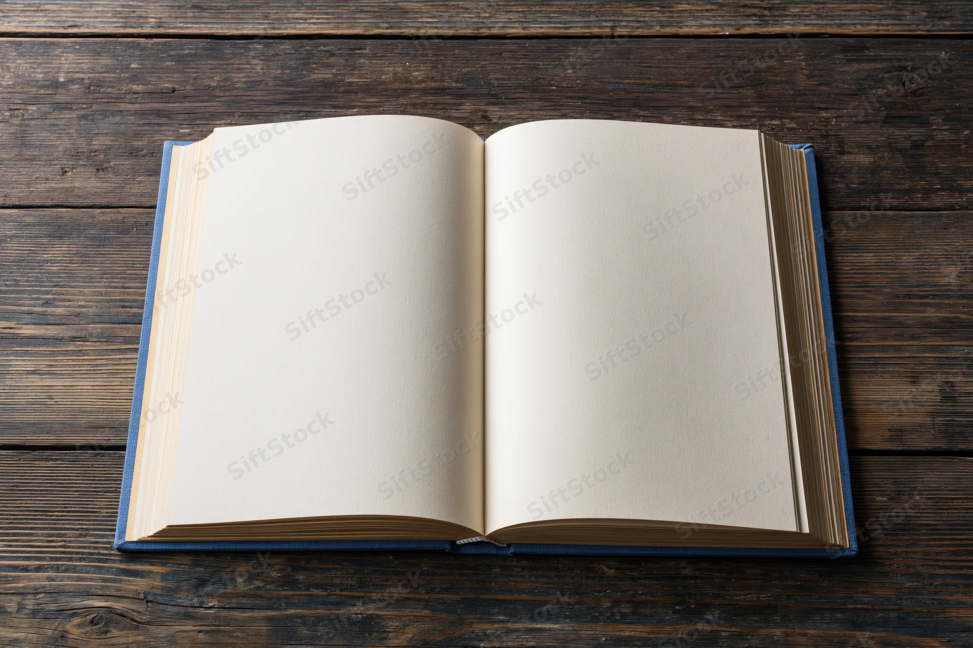 Open hardcover book with blank cream pages lying flat on dark wooden table