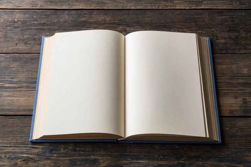 Open hardcover book with blank cream pages lying flat on dark wooden table