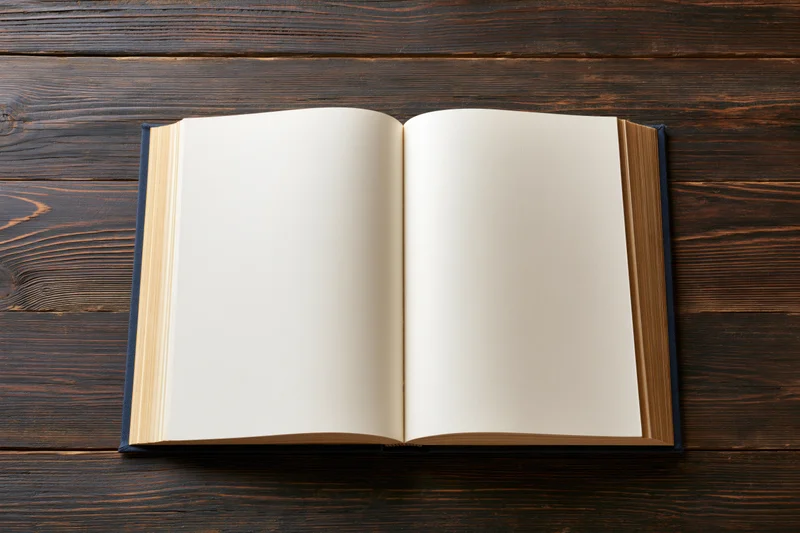 Open hardcover book with blank cream pages lying flat on dark wooden table
