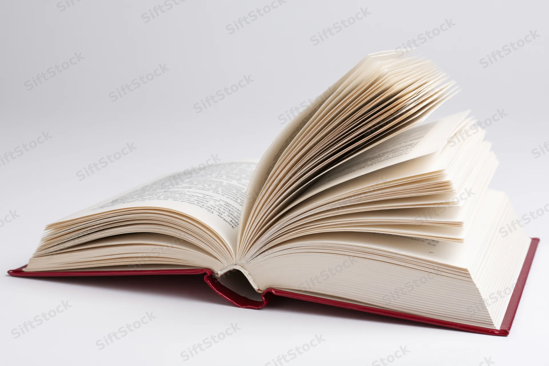 Open hardcover book with red binding lying flat and pages fanned on white background