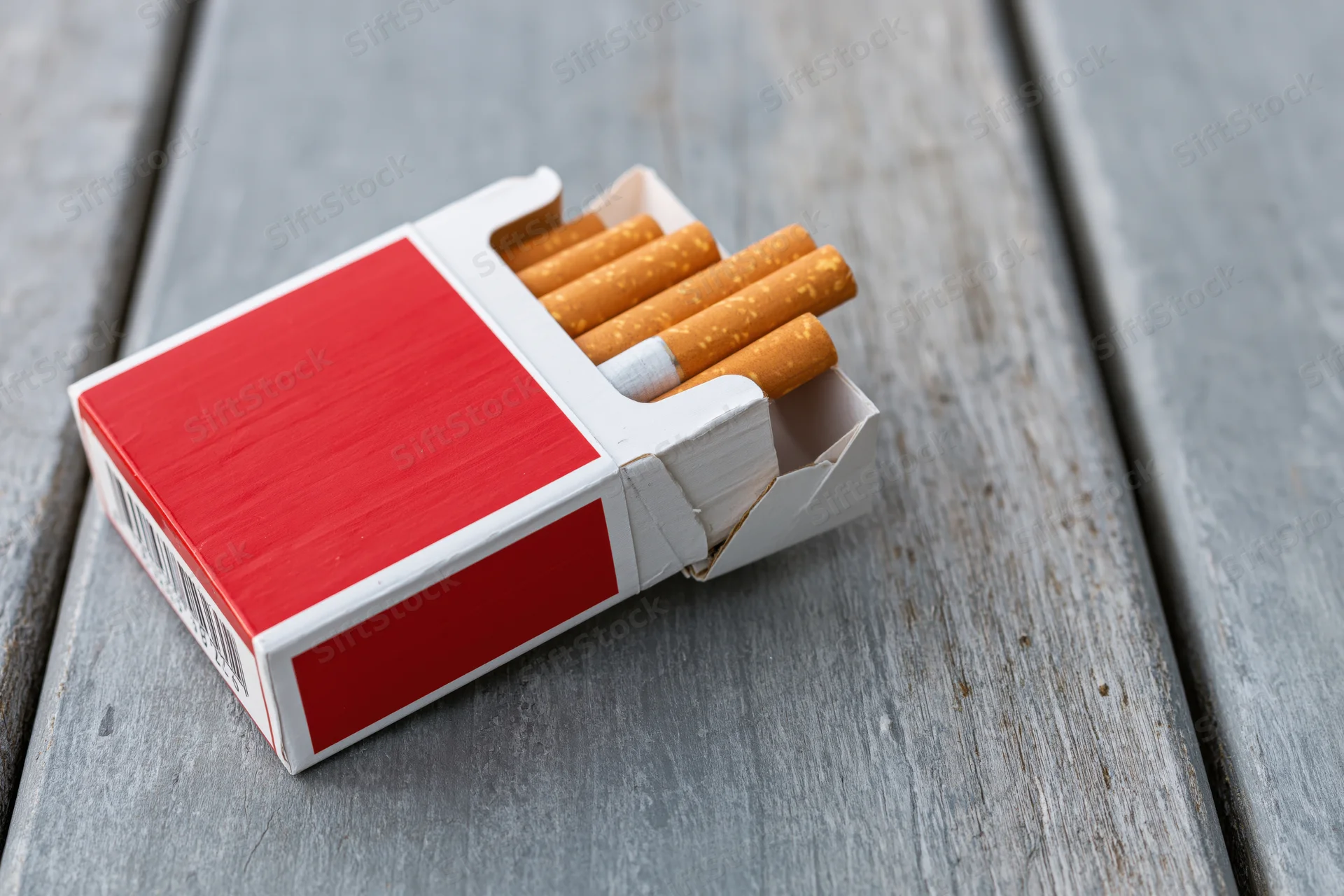 Open red and white cigarette pack with several cigarettes on a weathered wooden surface
