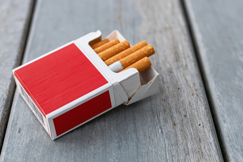 Open red and white cigarette pack with several cigarettes on a weathered wooden surface