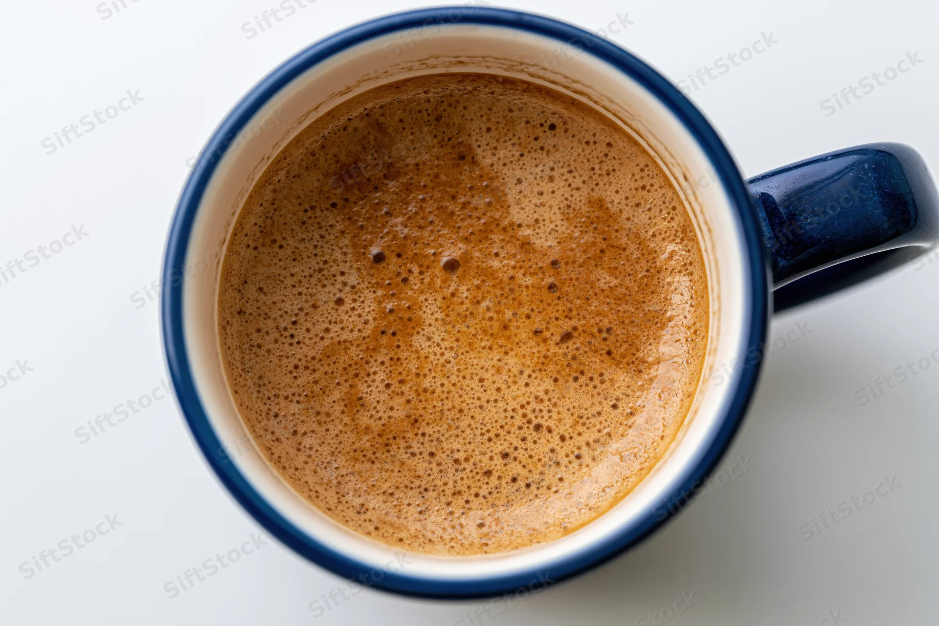 Overhead closeup of a ceramic coffee mug filled with foamy brown coffee on a white surface