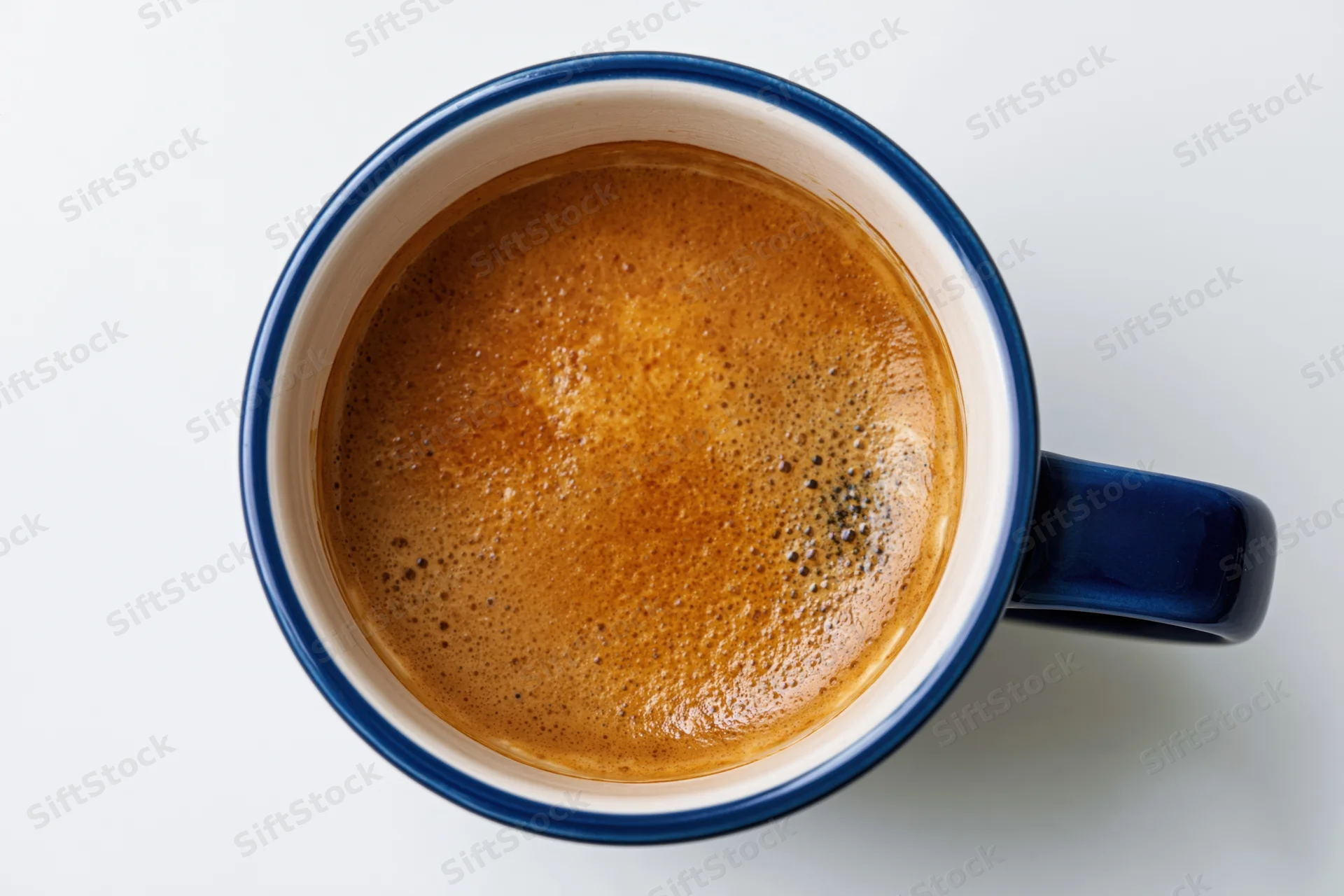 Overhead view of a blue ceramic coffee mug filled with frothy espresso on a white surface
