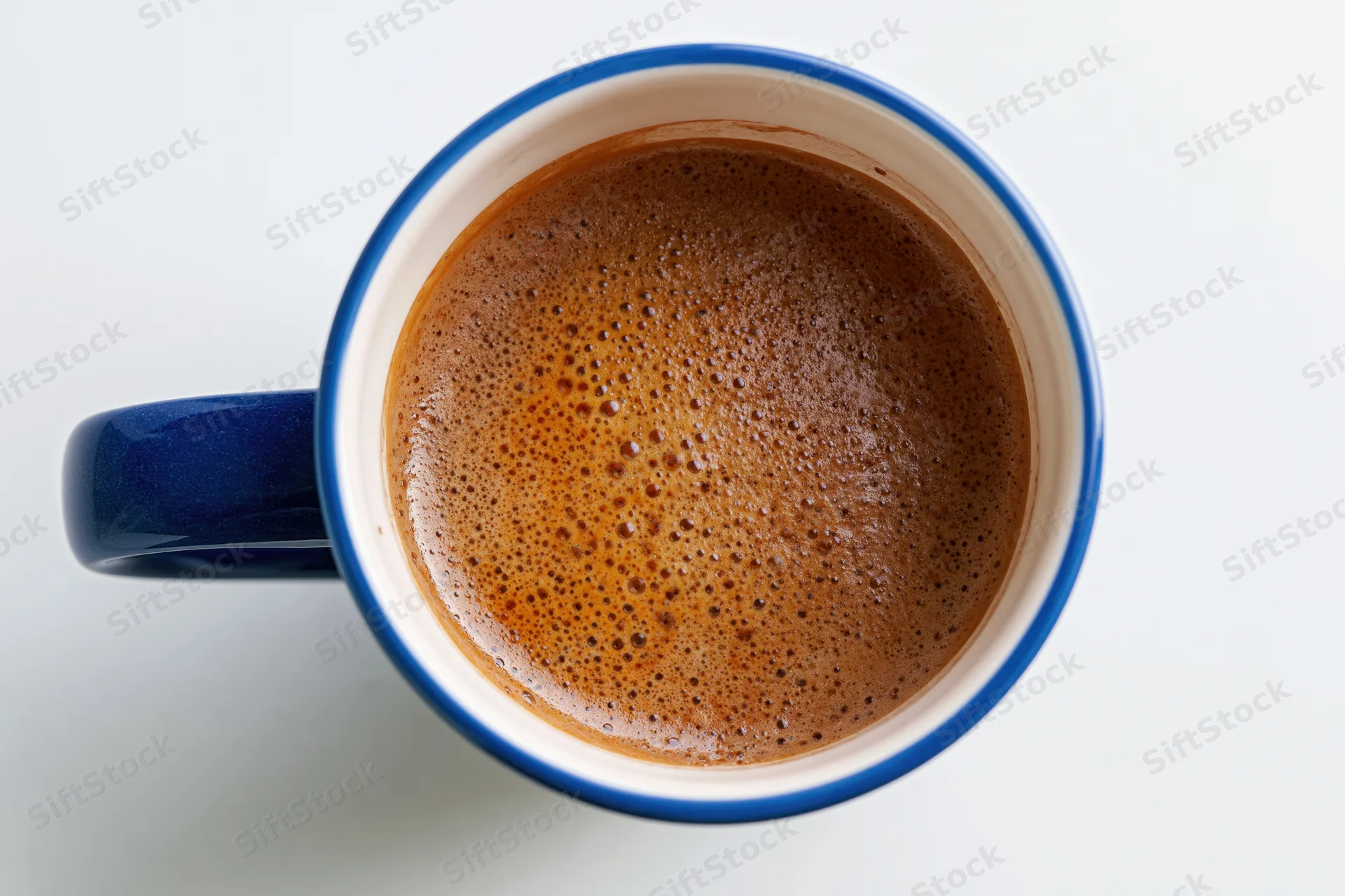 Overhead closeup of a blue ceramic coffee mug filled with frothy coffee on a white surface