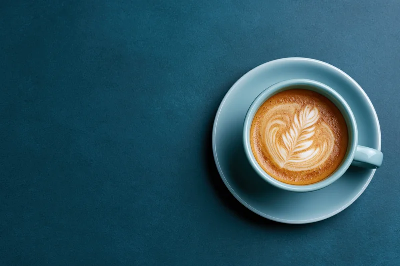 Light blue ceramic coffee cup with latte art on dark surface, overhead view
