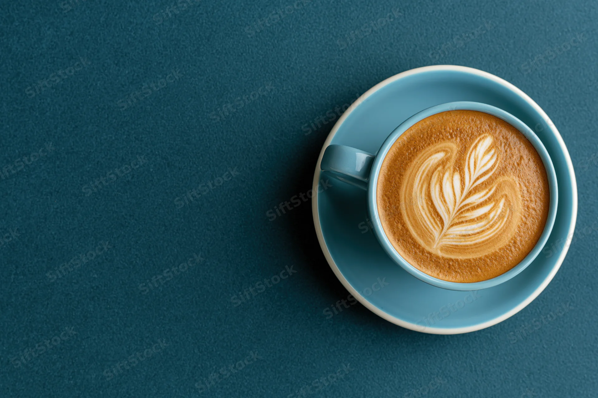 Overhead view of a blue ceramic coffee cup with latte art on a dark blue textured surface