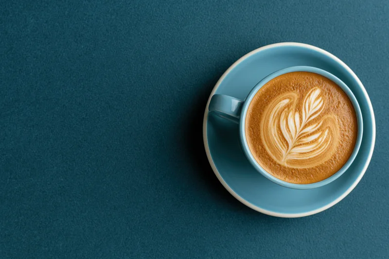 Overhead view of a blue ceramic coffee cup with latte art on a dark blue textured surface
