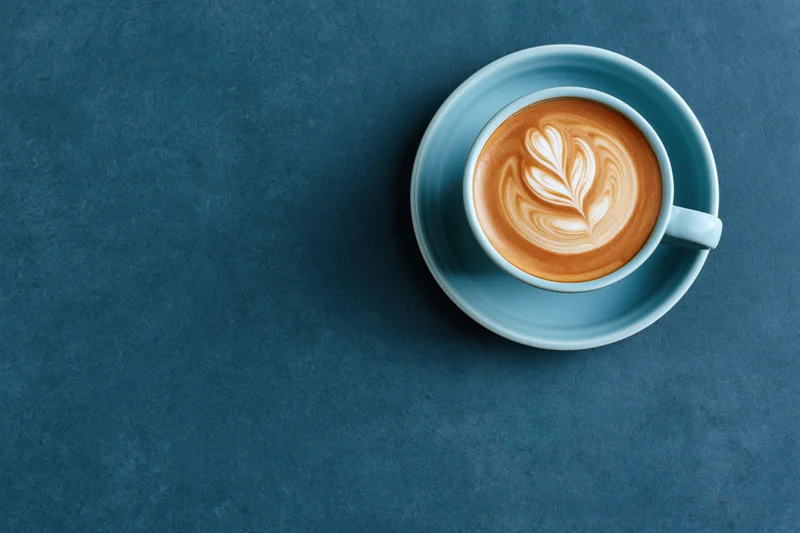 Light blue ceramic coffee cup with latte art on a dark blue surface, overhead view