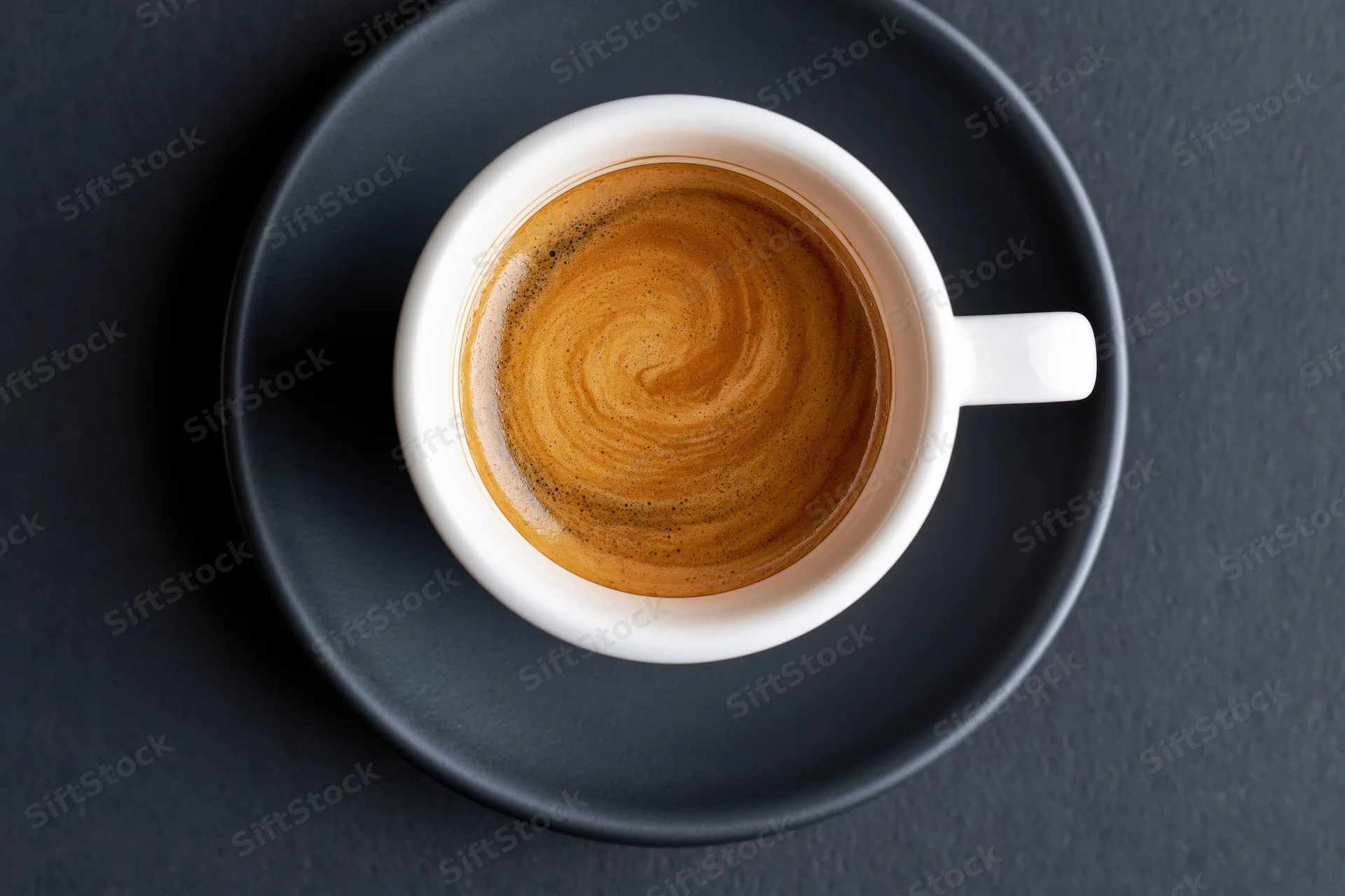 Overhead view of a white ceramic espresso cup with crema swirl on a dark saucer