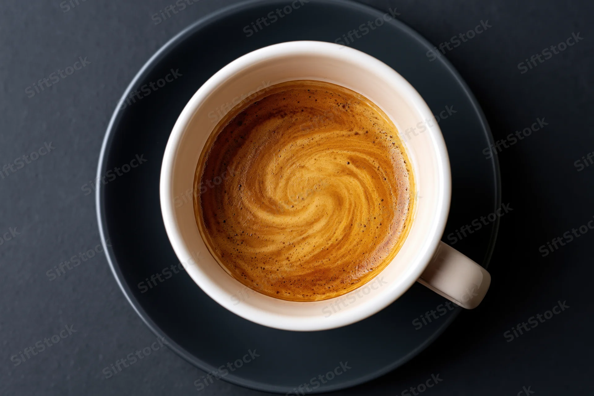 Overhead view of a white ceramic espresso cup with swirling crema on a dark saucer