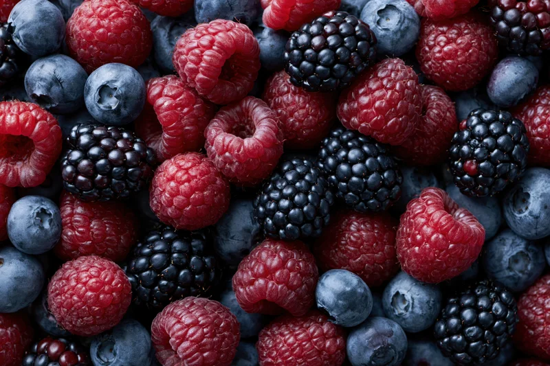 Overhead flat-lay of mixed fresh raspberries blueberries and blackberries filling the frame