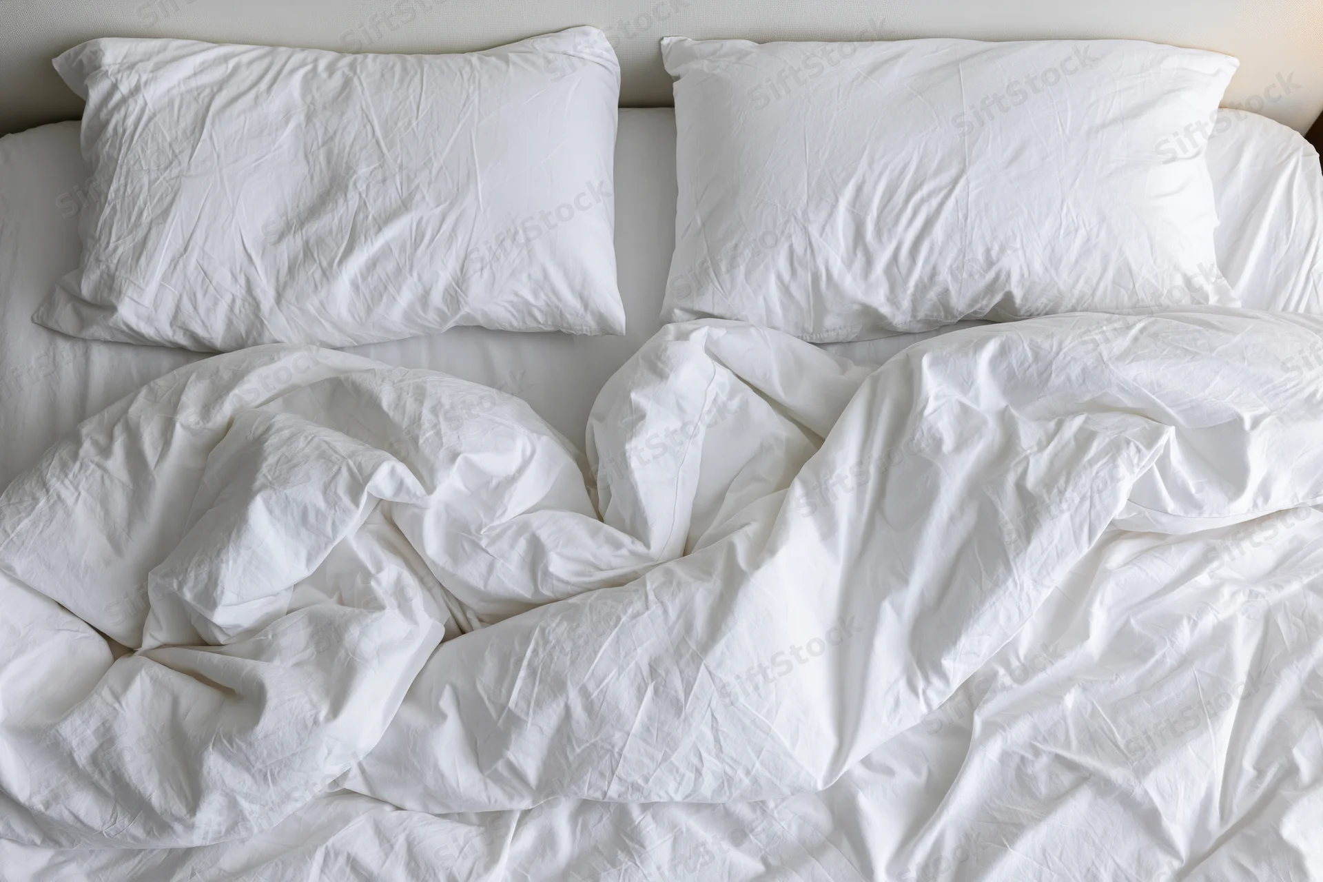 Overhead view of unmade bed with white crumpled sheets and two pillows in hotel room