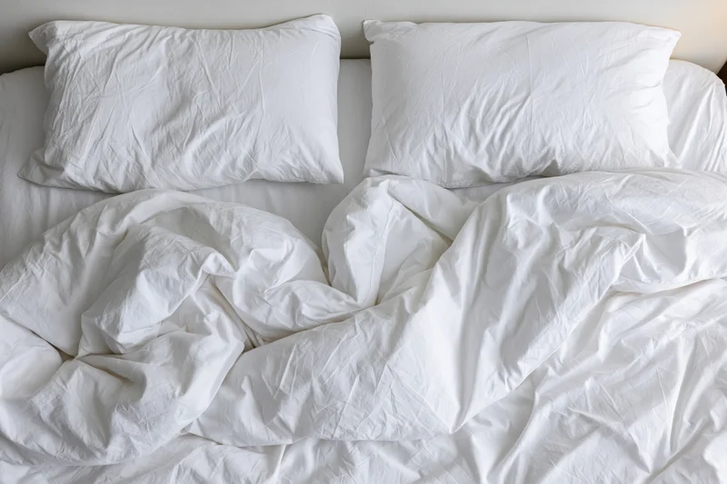 Overhead view of unmade bed with white crumpled sheets and two pillows in hotel room