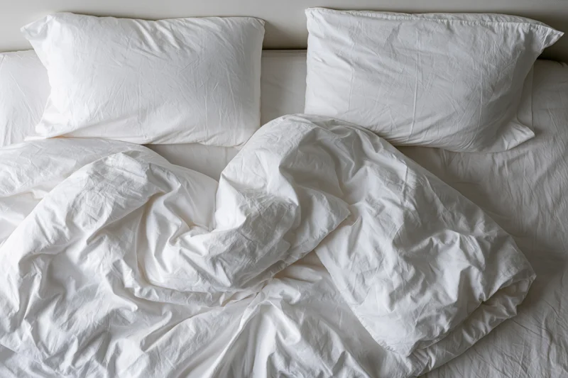 Overhead view of unmade white bed with crumpled sheets and two pillows in hotel room