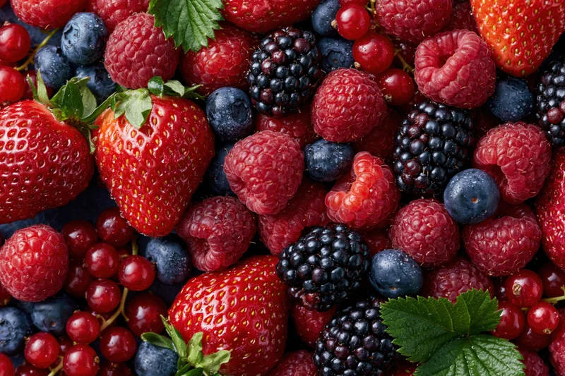 Overhead flat lay of mixed fresh berries including strawberries raspberries blueberries blackberries and redcurrants on a dark surface