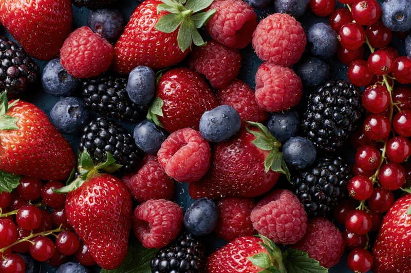 Overhead flat lay of mixed fresh berries including strawberries raspberries blueberries blackberries and redcurrants on dark surface