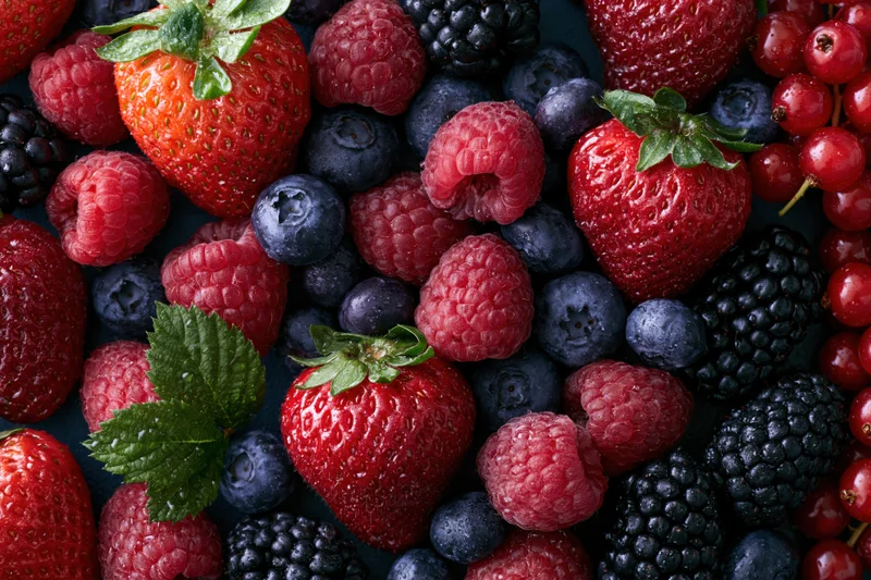 Overhead flat lay of mixed fresh berries including strawberries raspberries blueberries blackberries and redcurrants on dark surface