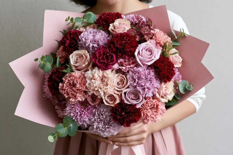 Woman holding a large lush bouquet of pink red and purple roses and carnations wrapped in paper
