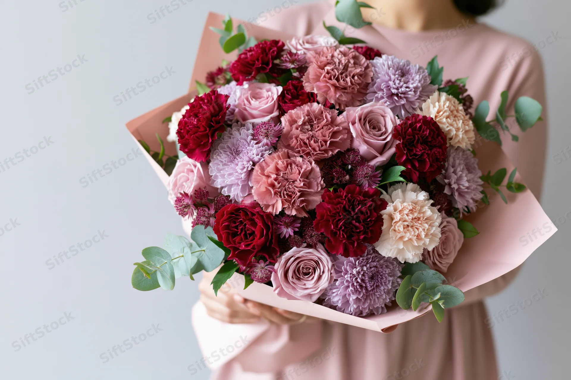 Woman holding a large lush bouquet of roses and carnations wrapped in pink paper