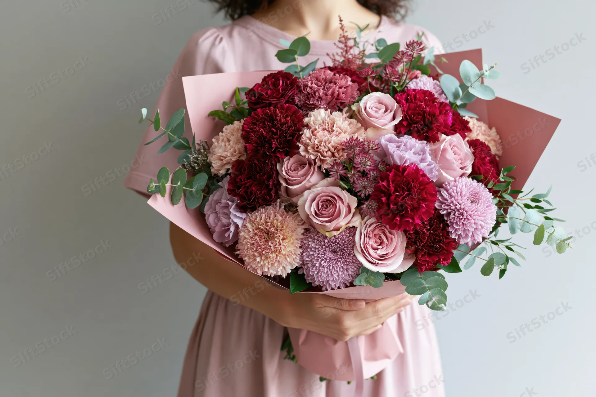 Woman holding a large lush bouquet of pink and red roses and carnations wrapped in pink paper