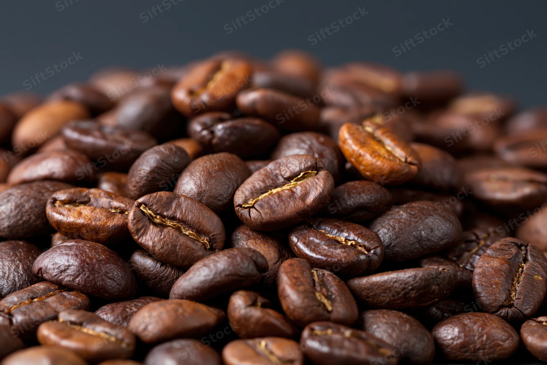 Closeup of roasted coffee beans piled on a dark surface