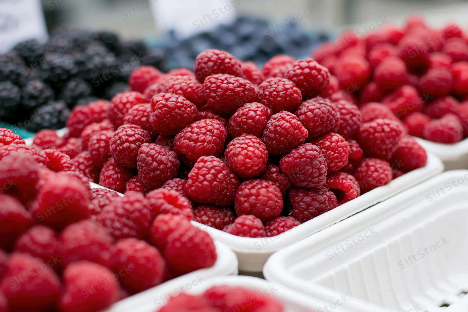 Fresh raspberries piled in white cardboard containers at a market stall